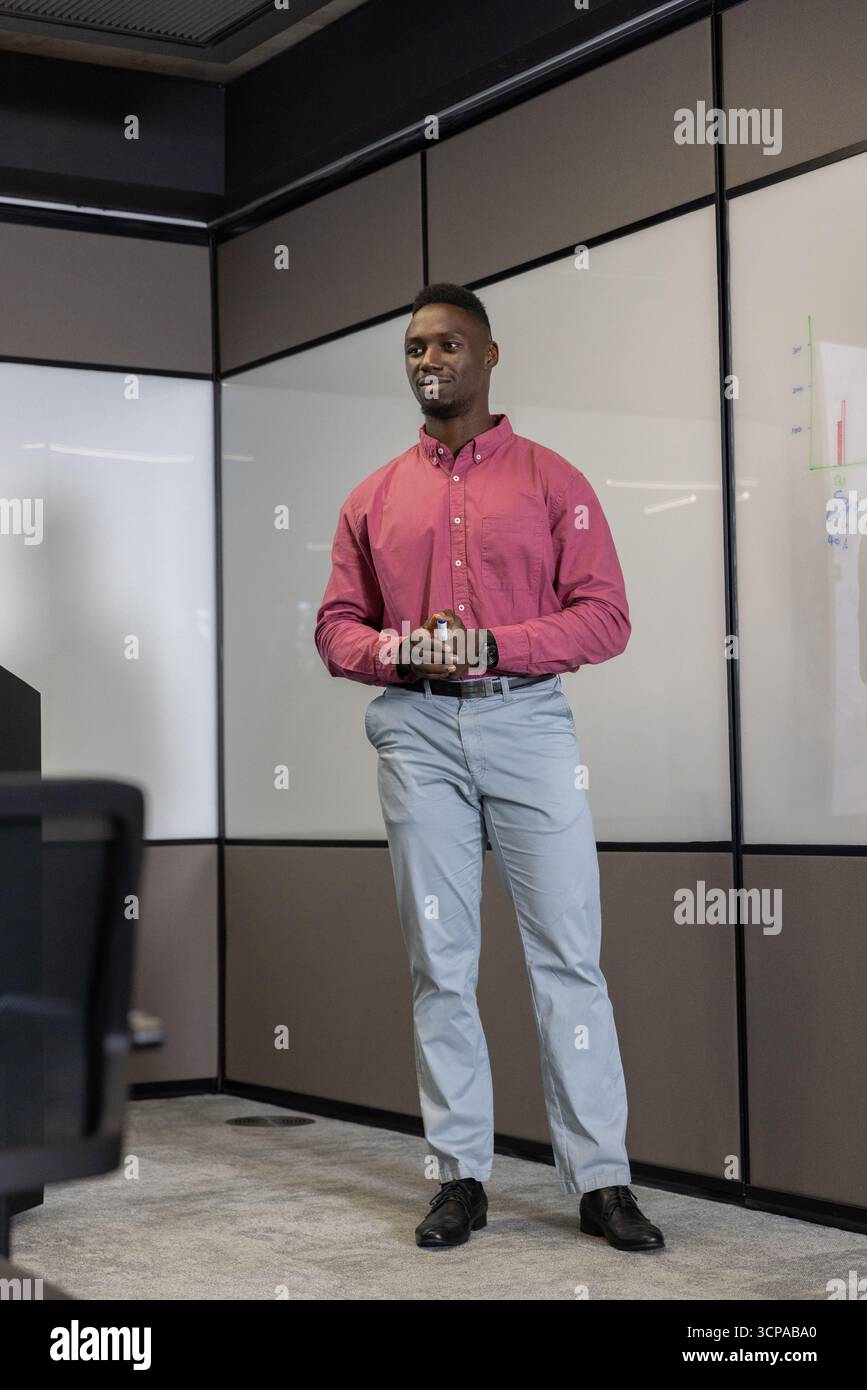 Uomo afroamericano in camicia che tiene il clicker e indica la carta sui pannelli della sala riunioni Foto Stock
