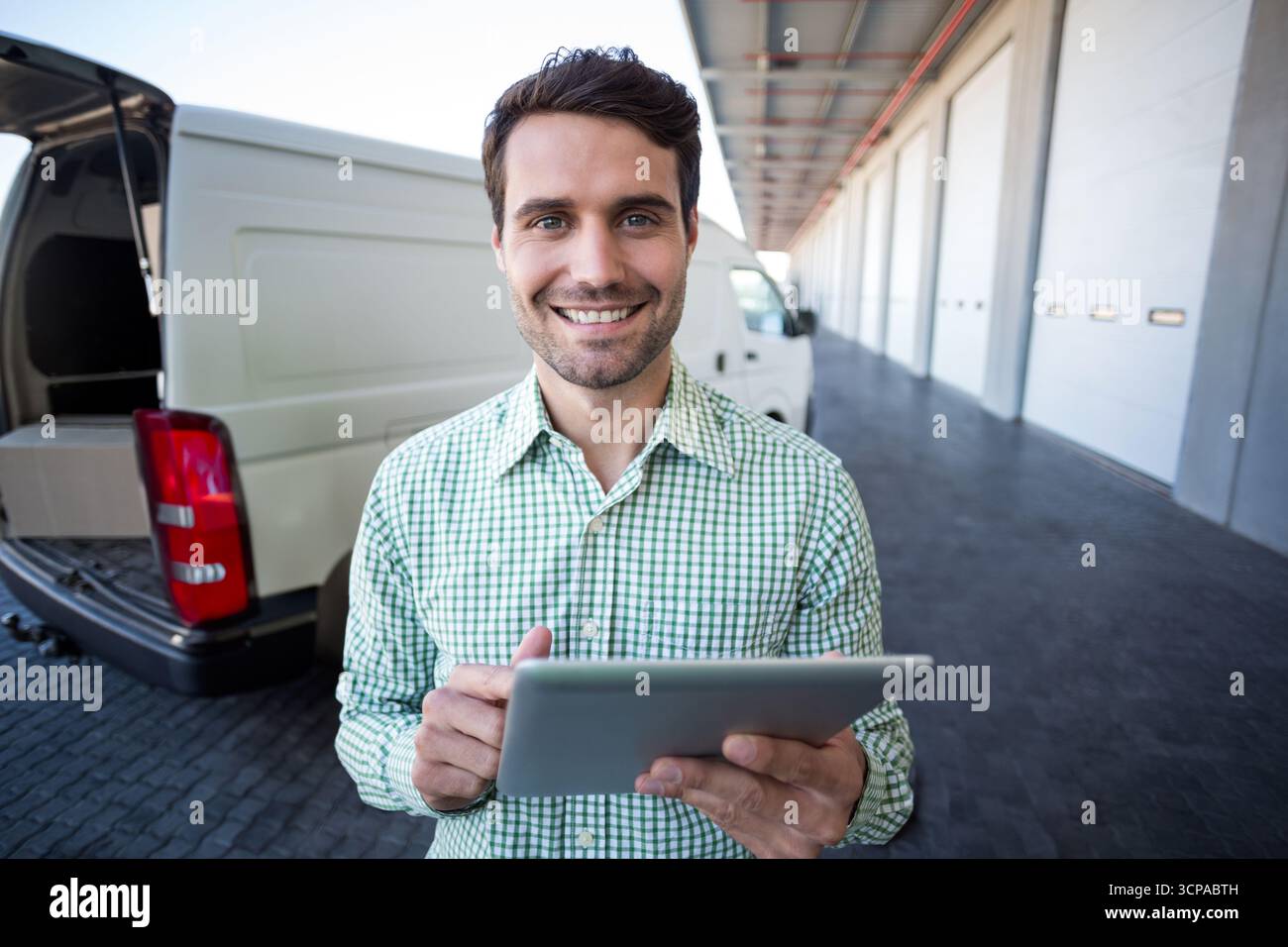 Furgone bianco in attesa al molo di carico con sportelli posteriori aperti che rivelano una scatola di cartone e un tablet Foto Stock