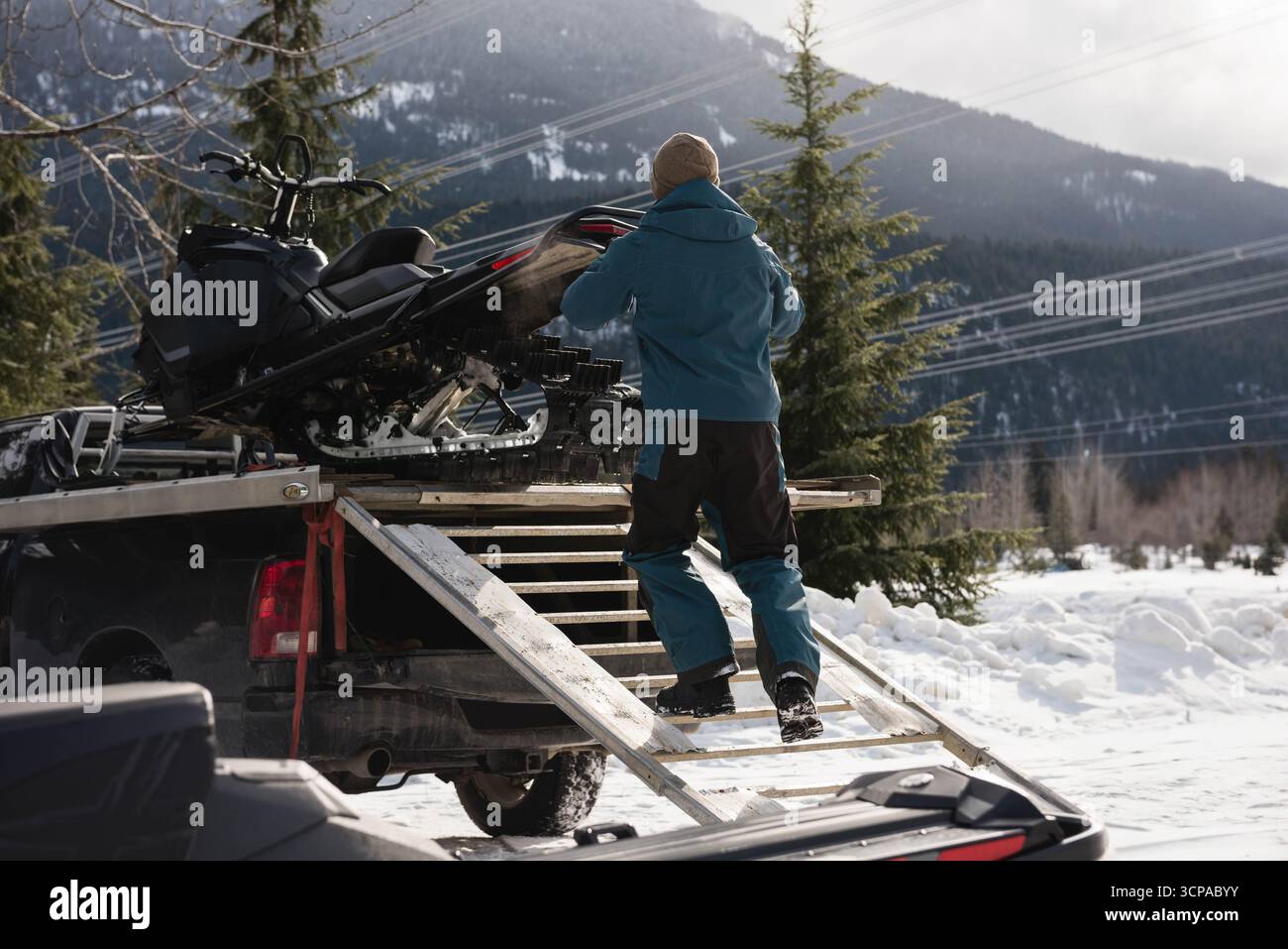 Uomo medio adulto in giacca invernale che guida la motoslitta su una rampa per il pick-up sul sentiero forestale Foto Stock