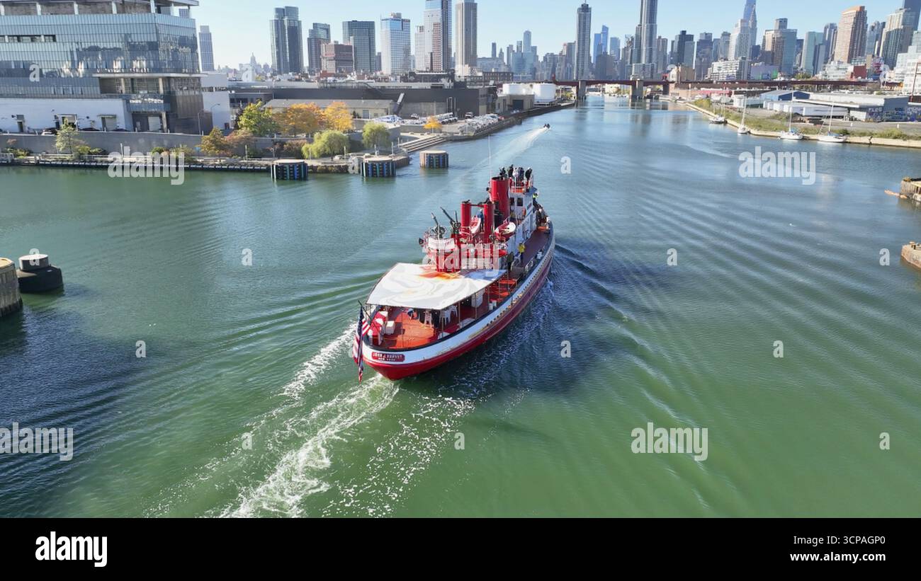 Brooklyn, Stati Uniti - 13 agosto 2023: Vista aerea di una vivace barca rossa che attraversa l'East River verso l'iconico skyline. Foto Stock