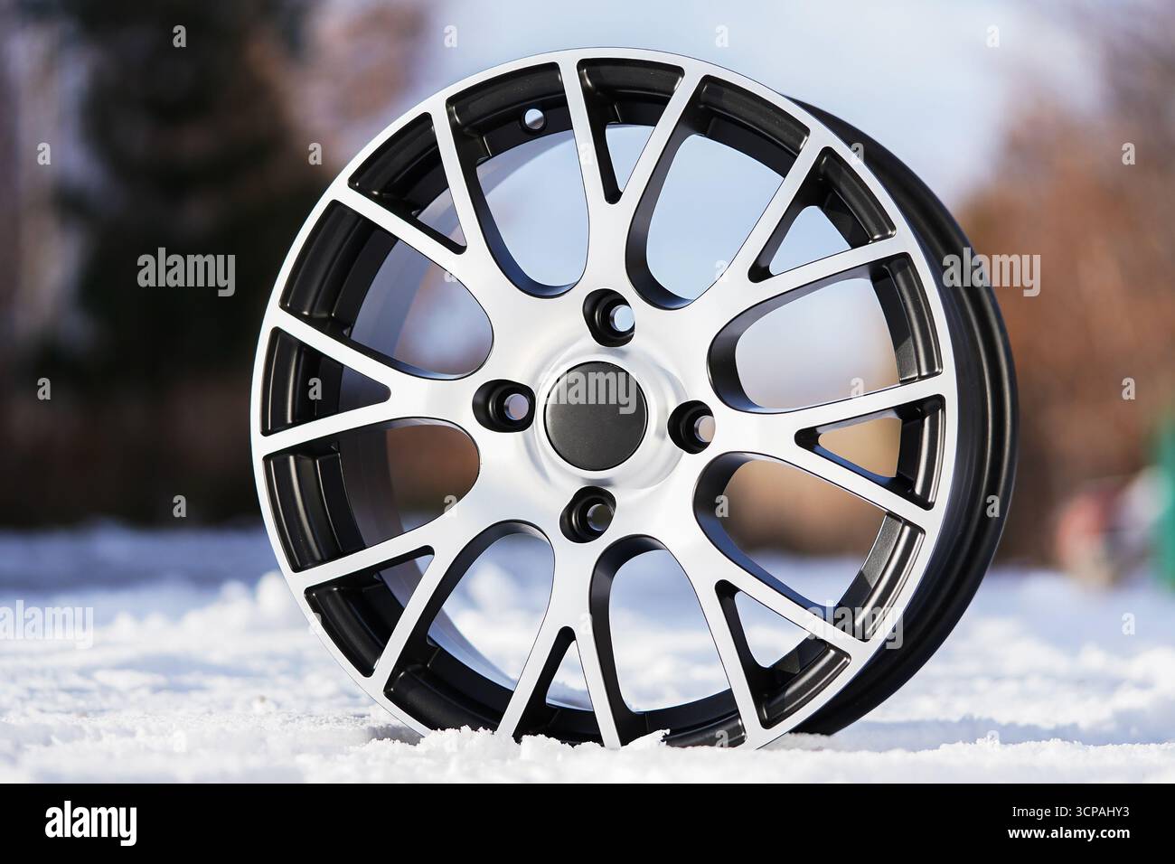 Un elegante cerchio in lega si erge in primo piano in un paesaggio innevato, evidenziando il suo design moderno e la sua maestria artigianale. La finitura lucida argento e nera Foto Stock