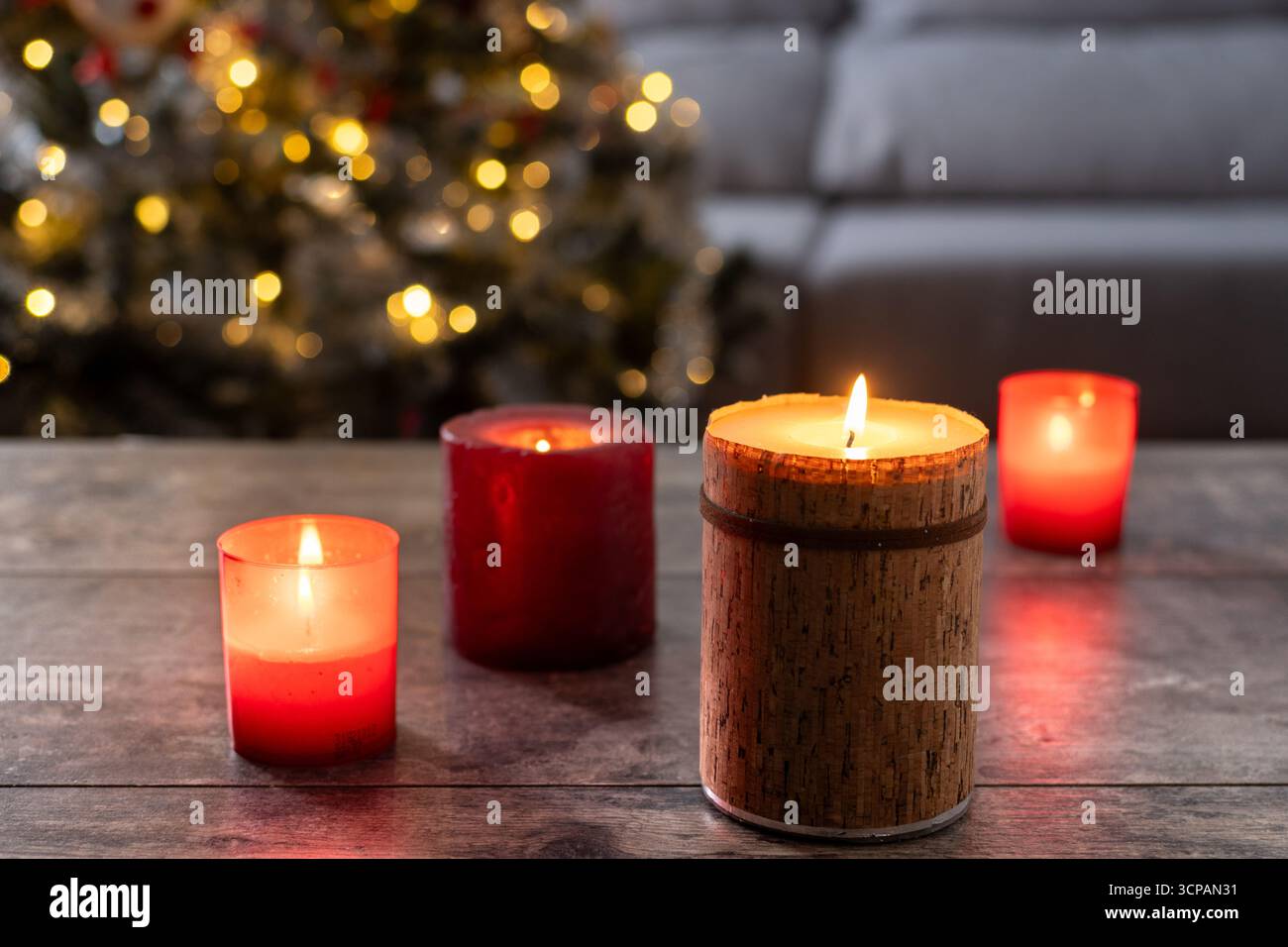 Candele rosse accese su un tavolo di legno con un albero di Natale sfocato e luci festose sullo sfondo. Accogliente atmosfera di vacanza e calda stagione de Foto Stock