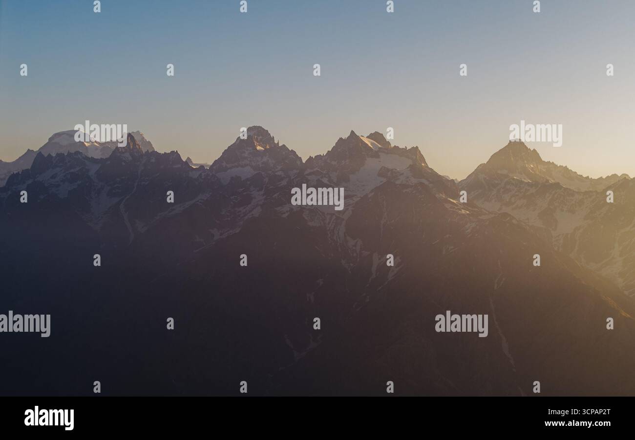 La vista aerea delle maestose cime innevate perfora il cielo mentre il sole proietta un bagliore dorato sul paesaggio aspro di Sosan, Himachal Pradesh, India. Foto Stock