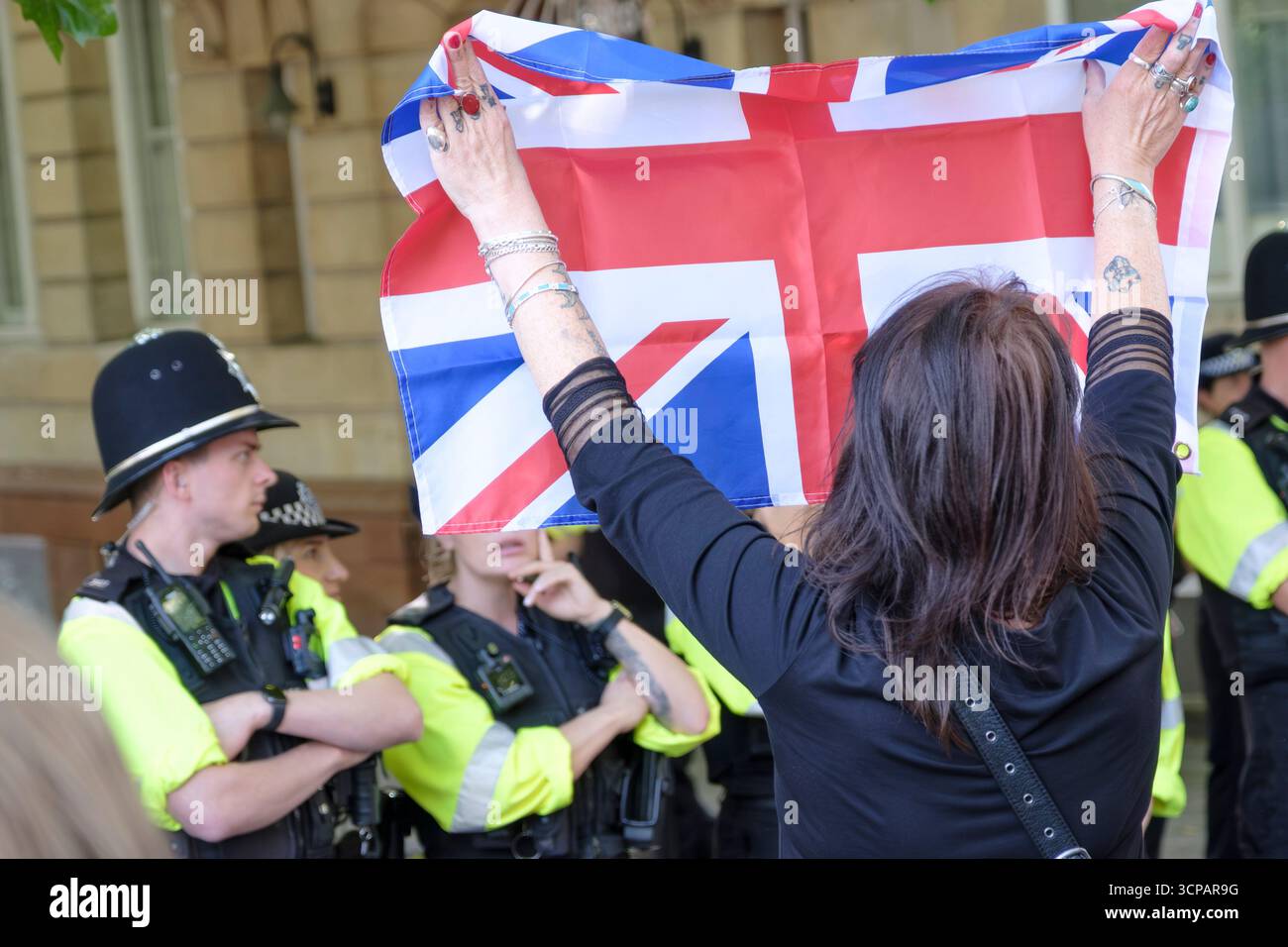 I manifestanti antifascisti e di estrema destra contro l'immigrazione di Bristol si sono urlati l'un l'altro tutto il pomeriggio a Castle Park Bristol, la polizia ha cercato di tenerli separati. Le donne con le braccia tatuate scherzano i rifugiati sono le benvenute contro la protesta con la bandiera dell'unione Foto Stock