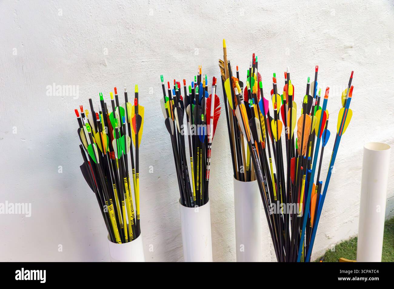 Frecce dai colori vivaci confezionate in provette di plastica bianca appoggiate su una parete semplice e pronte per l'uso con messa a fuoco selettiva Foto Stock