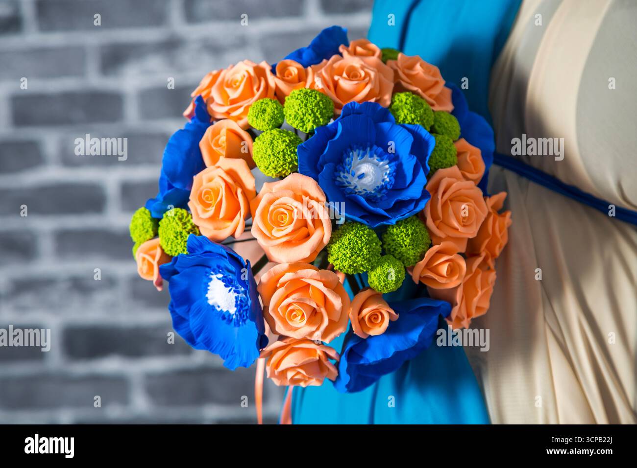 Un bouquet di fiori con fiori azzurri e arancioni. I fiori sono disposti in un vaso e il bouquet è tenuto da una donna. I fiori sono colorati e. Foto Stock