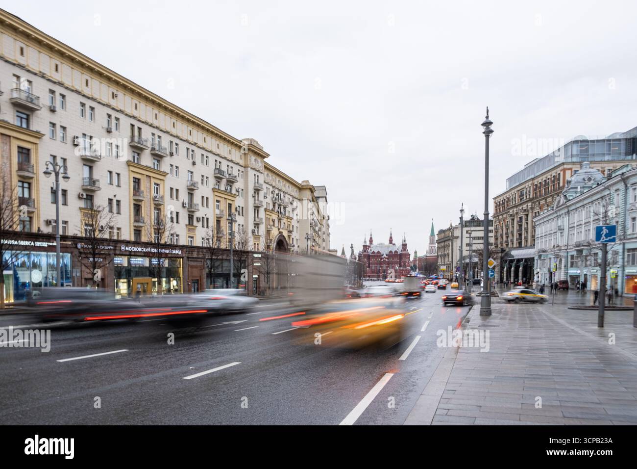 Un'immagine sfocata di una strada trafficata con auto e pedoni. La scena è movimentata e vivace, con le auto e le persone che si muovono rapidamente attraverso la città Foto Stock