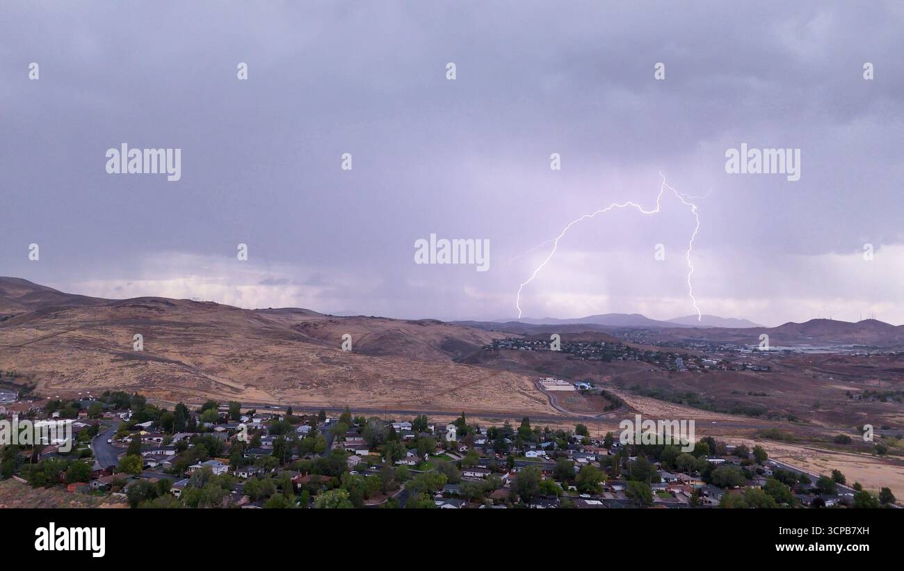 La vista aerea di un potente fulmine illumina le lontane colline oltre la città, contrastando il cielo tempestoso sopra, Prescott, Arizona, Stati Uniti. Foto Stock