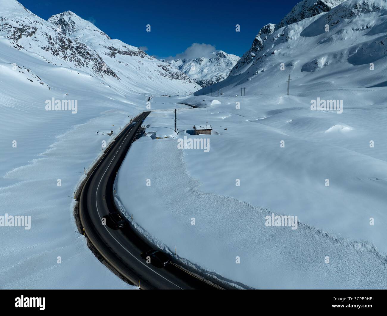 Veduta aerea di una strada tortuosa che taglia la neve bianca del passo Julier, sotto lo sguardo vigile di montagne torreggianti e frastagliate, passo Julier, Grigioni, Svizzera. Foto Stock