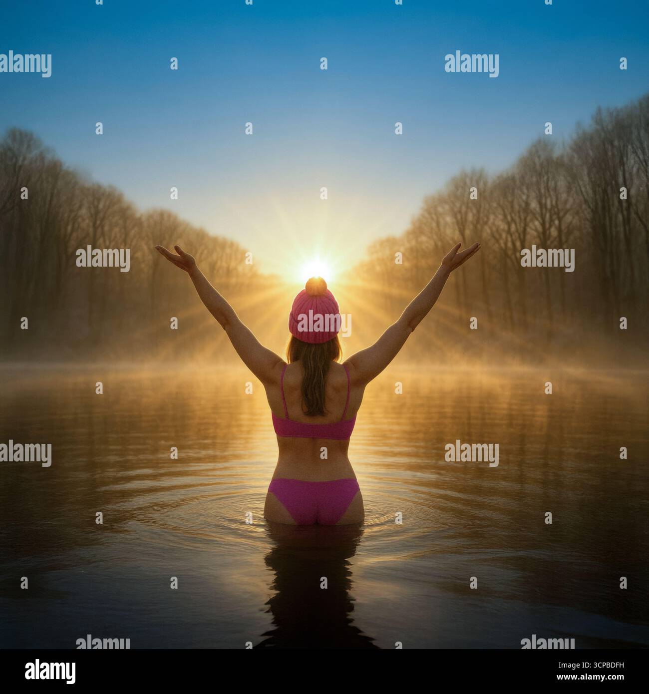 Una donna con un bikini rosa e un cappello da bobble alza le braccia verso il sole, abbracciando la gioia di un tuffo d'acqua fredda all'alba. Foto Stock
