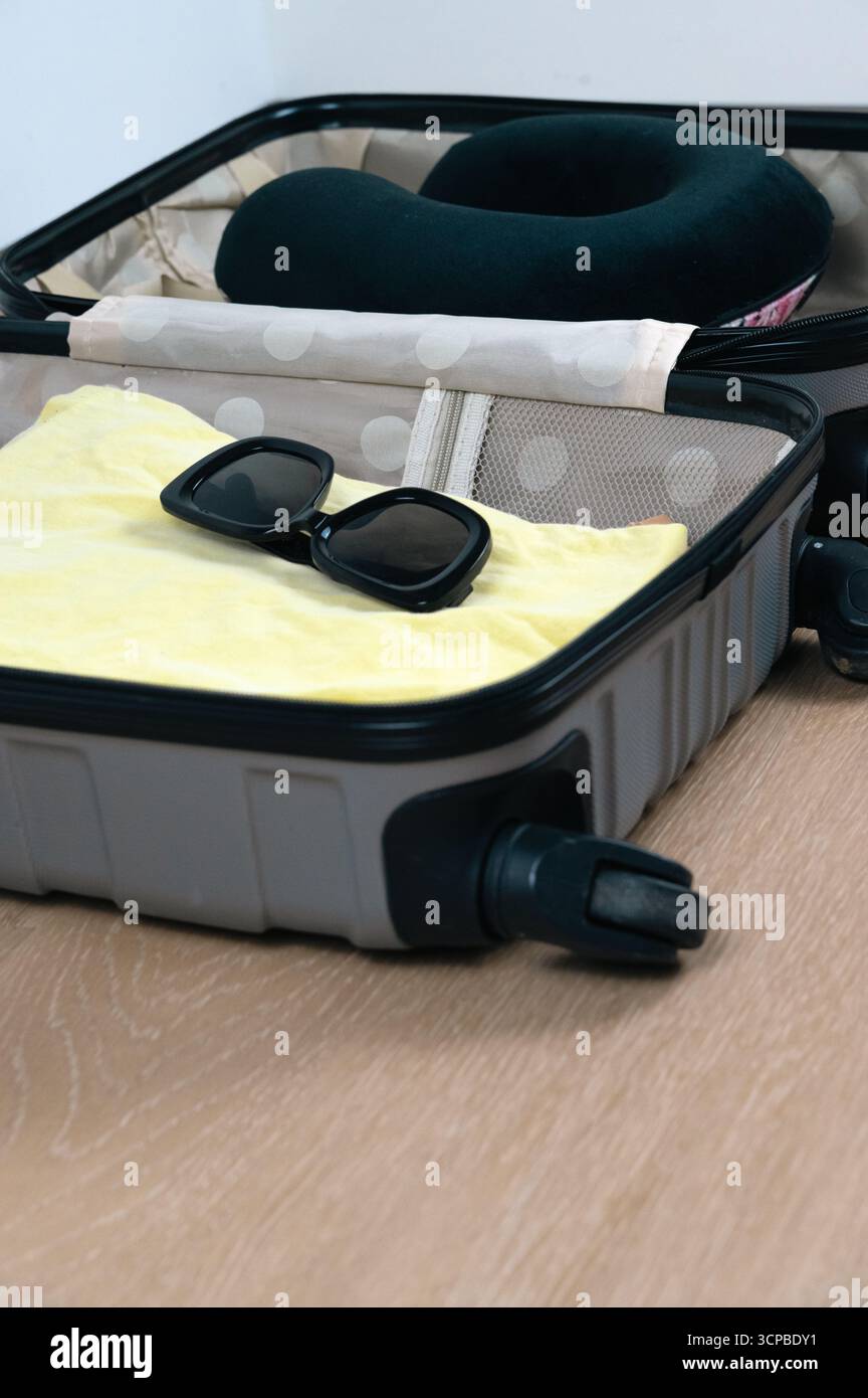 Un'elegante valigia piena di accessori da viaggio come occhiali da sole e un cuscino da viaggio per il massimo comfort durante il viaggio Foto Stock