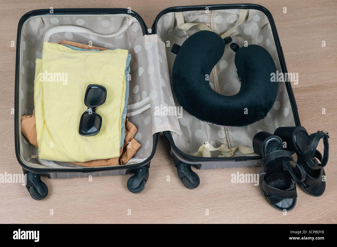 Una valigia colorata piena di abbigliamento, occhiali da sole, un cuscino per il collo e sandali per un viaggio emozionante Foto Stock
