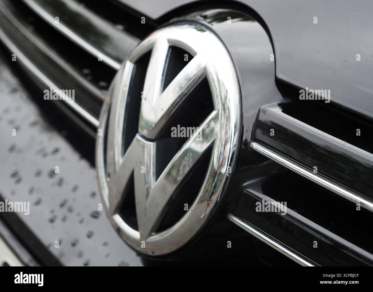 Vilshofen sul Danubio, Germania. 25 settembre 2025. Il logo Volkswagen, una "VW" cromata all'interno di un cerchio, posta contro la calandra nera di un'auto. Il logo è altamente riflettente e mostra una sorgente luminosa morbida e diffusa. Le gocce d'acqua sono visibili sul cromo e sulla griglia in plastica, aggiungendo texture e realismo all'immagine. Credito: SOPA Images Limited/Alamy Live News Foto Stock