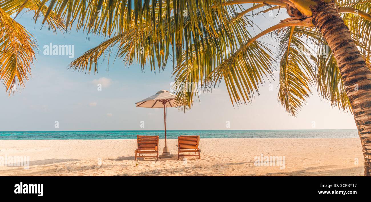 Spiaggia felice e rilassante al tramonto, due sedie a sdraio, ombrellone, foglie di palma. Splendida destinazione per le vacanze estive, vista panoramica del cielo di sabbia marina, ora d'oro. Foto Stock