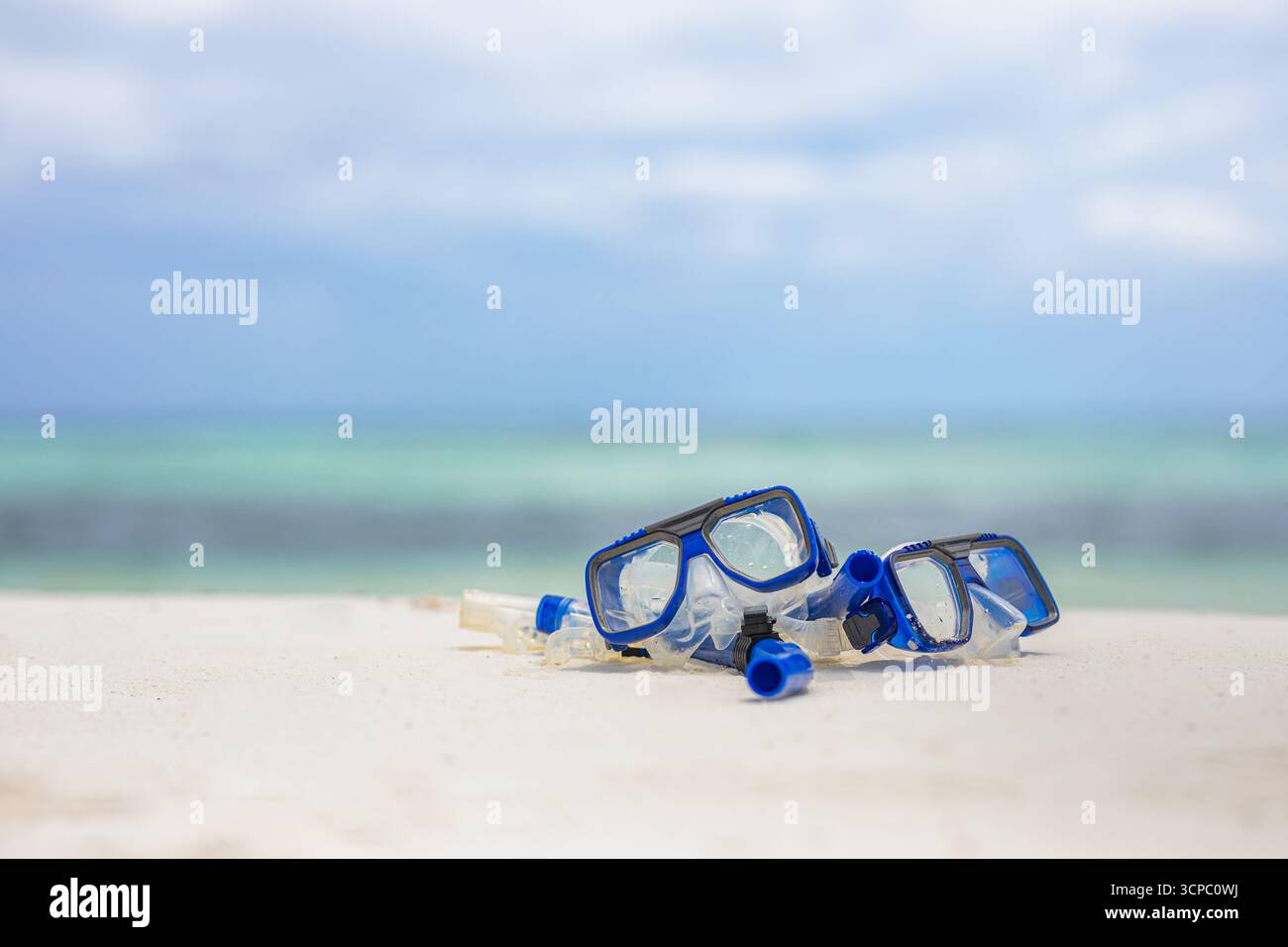 Primo piano dell'attrezzatura da snorkeling sulla spiaggia estiva. Maschera, boccaglio attività ricreative all'aperto. Mare, cielo e orizzonte sfocati. Natura morta astratta in sabbia soleggiata Foto Stock