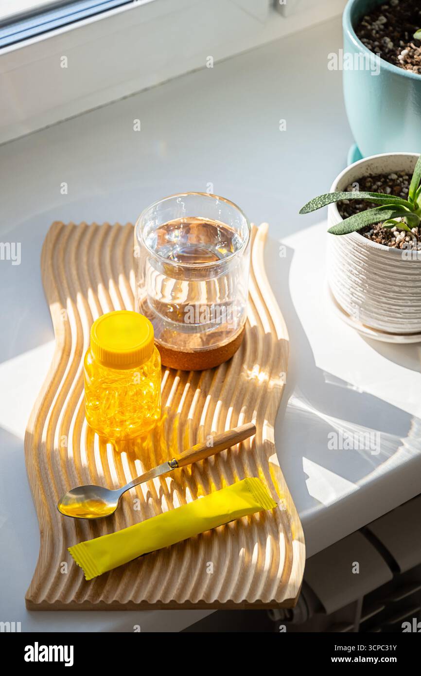 Bottiglia di vitamine gialle, cucchiaio, bicchiere d'acqua, sacchetto di polvere su tavola di legno. Concetto di integratore alimentare. Foto Stock
