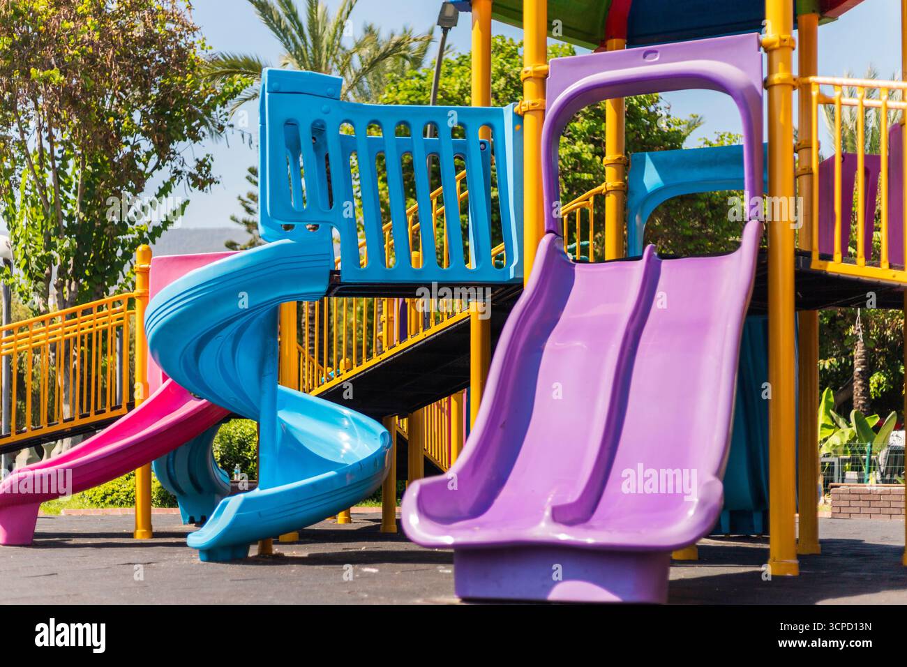 I bambini possono divertirsi giocando su scivoli colorati in un parco giochi luminoso circondato dal verde in un pomeriggio di sole, per un'emozionante giornata all'aria aperta Foto Stock