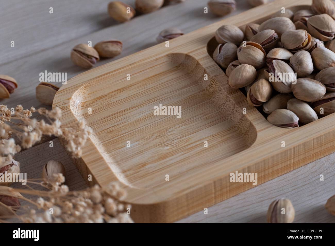 Una vista dall'alto verso il basso di pistacchi rustici sgusciati su un vassoio di legno, sparsi su una superficie di legno chiaro, evidenziando texture naturali e toni terrosi Foto Stock