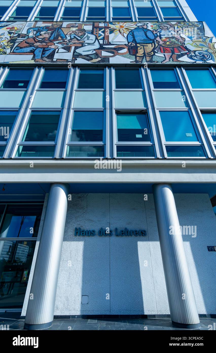Angolo verticale dell'ingresso della Haus des Lehrers a Berlino, con opere d'arte a mosaico e colonne iconiche sotto il cielo limpido. Foto Stock