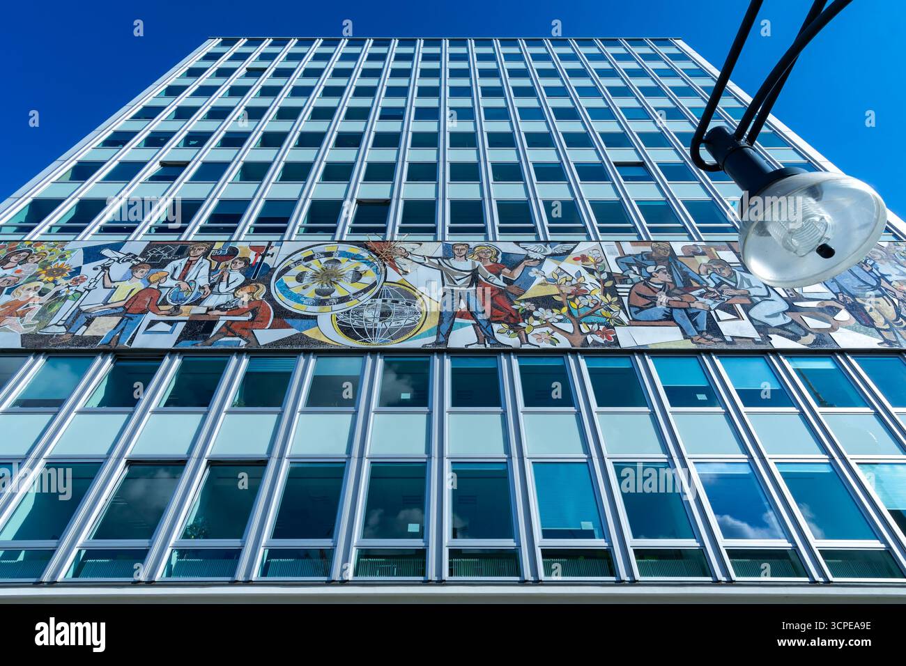 Vista dall'angolo basso della Haus des Lehrers a Berlino con iconico fregio a mosaico socialista e lampione stradale in primo piano. Foto Stock