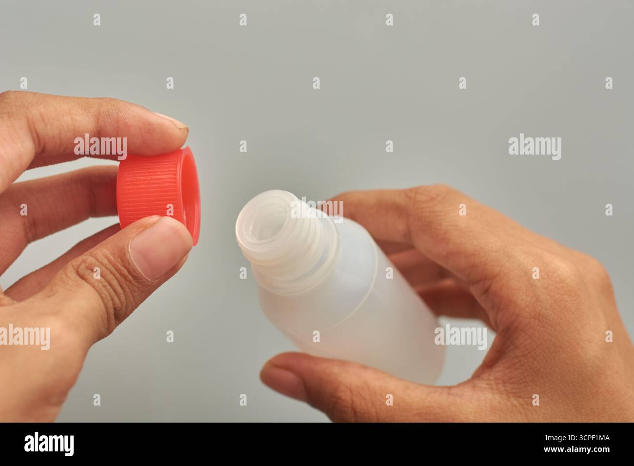 apertura o svitamento delle mani tappo scanalato rosso su un piccolo flacone in plastica bianca traslucida, accesso a medicinali o rimedi, sfondo grigio isolato Foto Stock