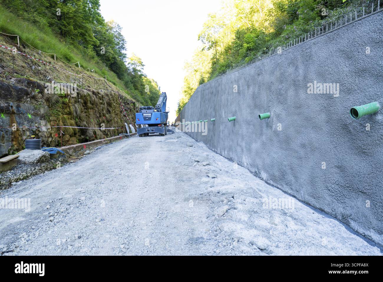 Muro di cemento in cantiere con gru blu, circondato da boschi e sentieri di ghiaia, cantiere Hermann Hessebahn, Calw, Germania Foto Stock