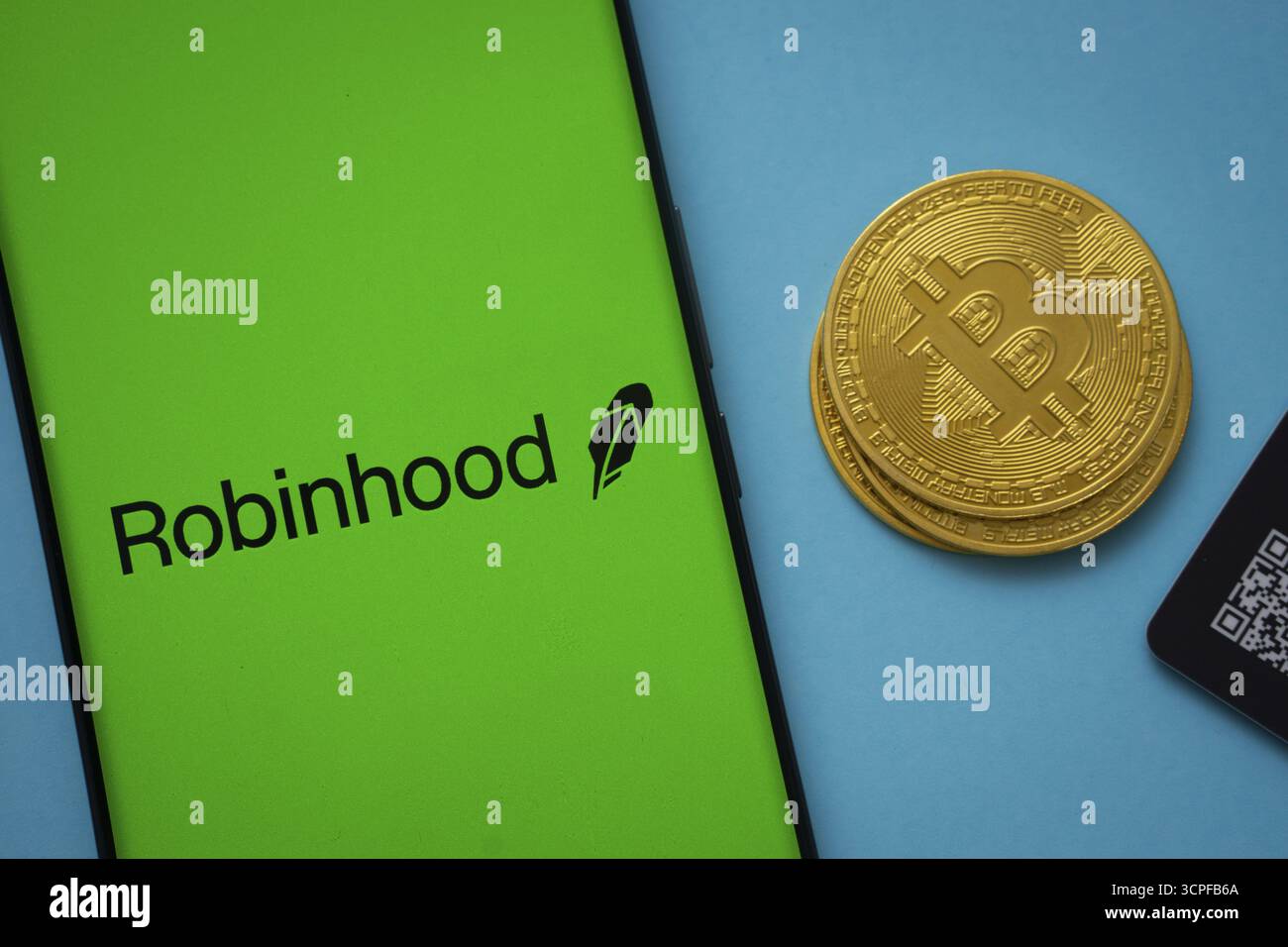 Dhaka, Bangladesh- 26 agosto 2025: Logo Robinhood sullo schermo dello smartphone vicino alla moneta Bitcoin e codice QR su sfondo blu Foto Stock