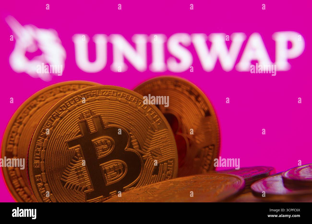 Dhaka, Bangladesh - 09 settembre 2025: Primo piano delle monete Bitcoin con il logo Uniswap visibile su uno schermo sullo sfondo Foto Stock