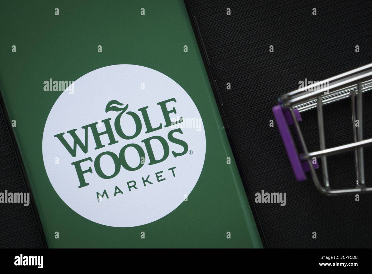 Dhaka, Bangladesh - 3 luglio 2025: Uno smartphone con il logo Whole Foods Market accanto a un carrello in miniatura sullo sfondo Foto Stock