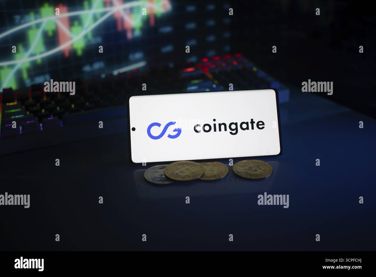 Telefono con logo Coingate, sullo sfondo di monitor e monete commerciali Foto Stock
