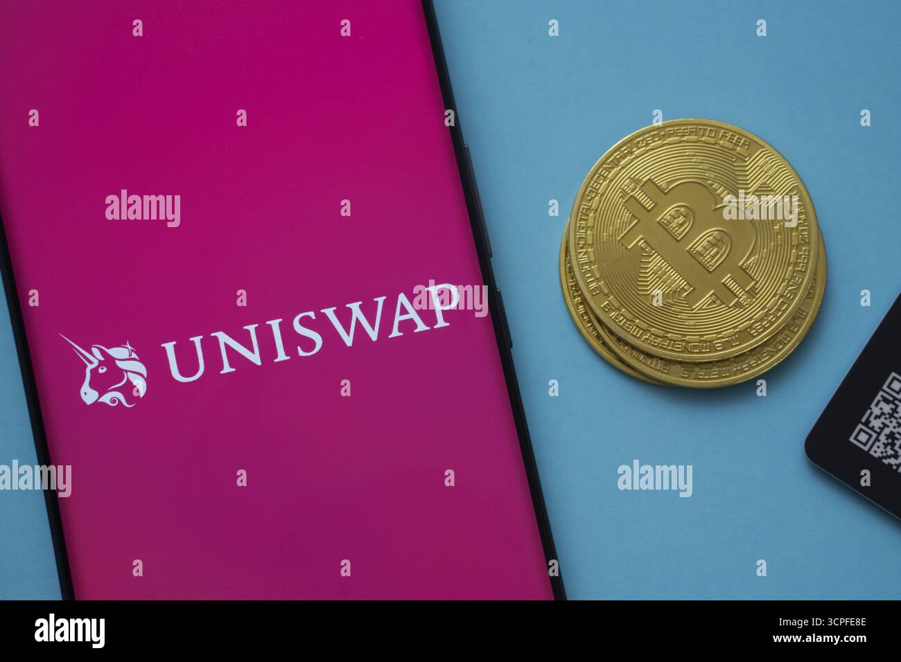Dhaka, Bangladesh - 19 settembre 2025: Logo Uniswap sullo schermo dello smartphone vicino alla moneta Bitcoin e codice QR su sfondo blu Foto Stock