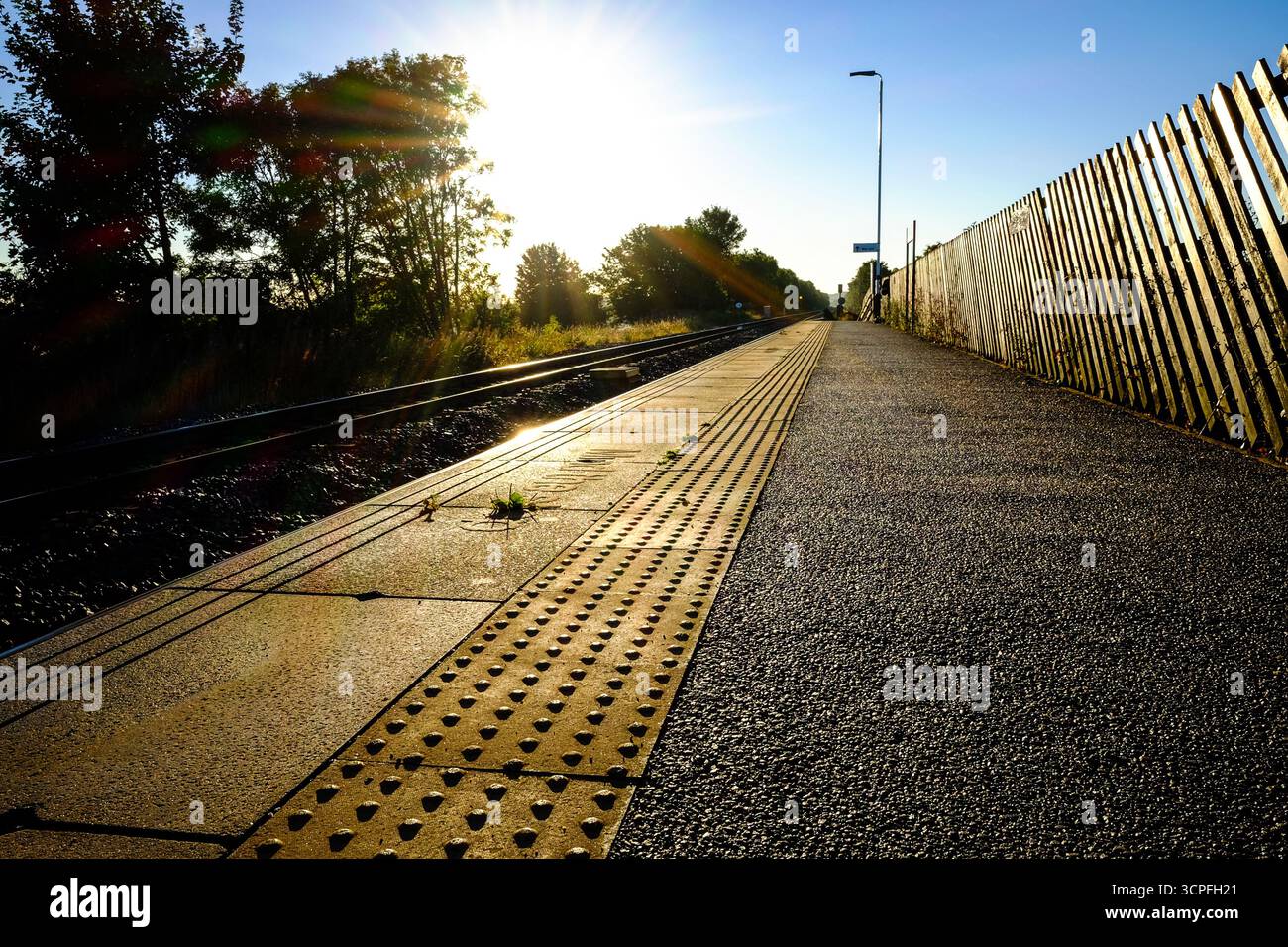 Vista dell'alba lungo una piattaforma ferroviaria vuota con binari e pavimentazione tattile Foto Stock