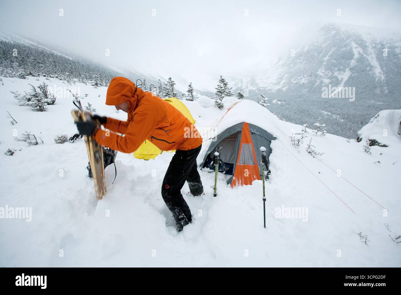 Un uomo solleva gli sci dalla neve profonda di fronte alla sua tenda da campeggio sul Monte Washington. Foto Stock