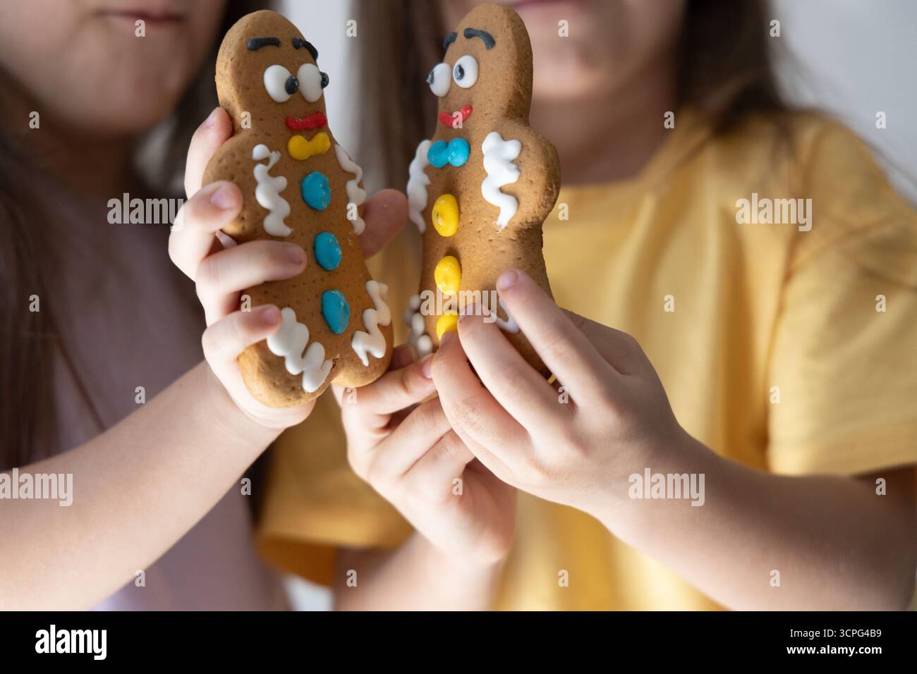 Due bambini tengono i biscotti dell'uomo di pan di zenzero vicini l'uno all'altro. Festività natalizie con bambini e dolciumi al forno che simboleggiano il Natale e. Foto Stock