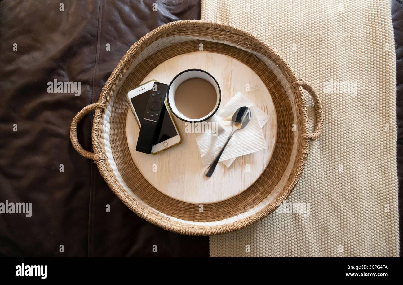 Vista dall'alto del cestino abbronzato su mobili che reggono tazza, telecomando, telefono Foto Stock