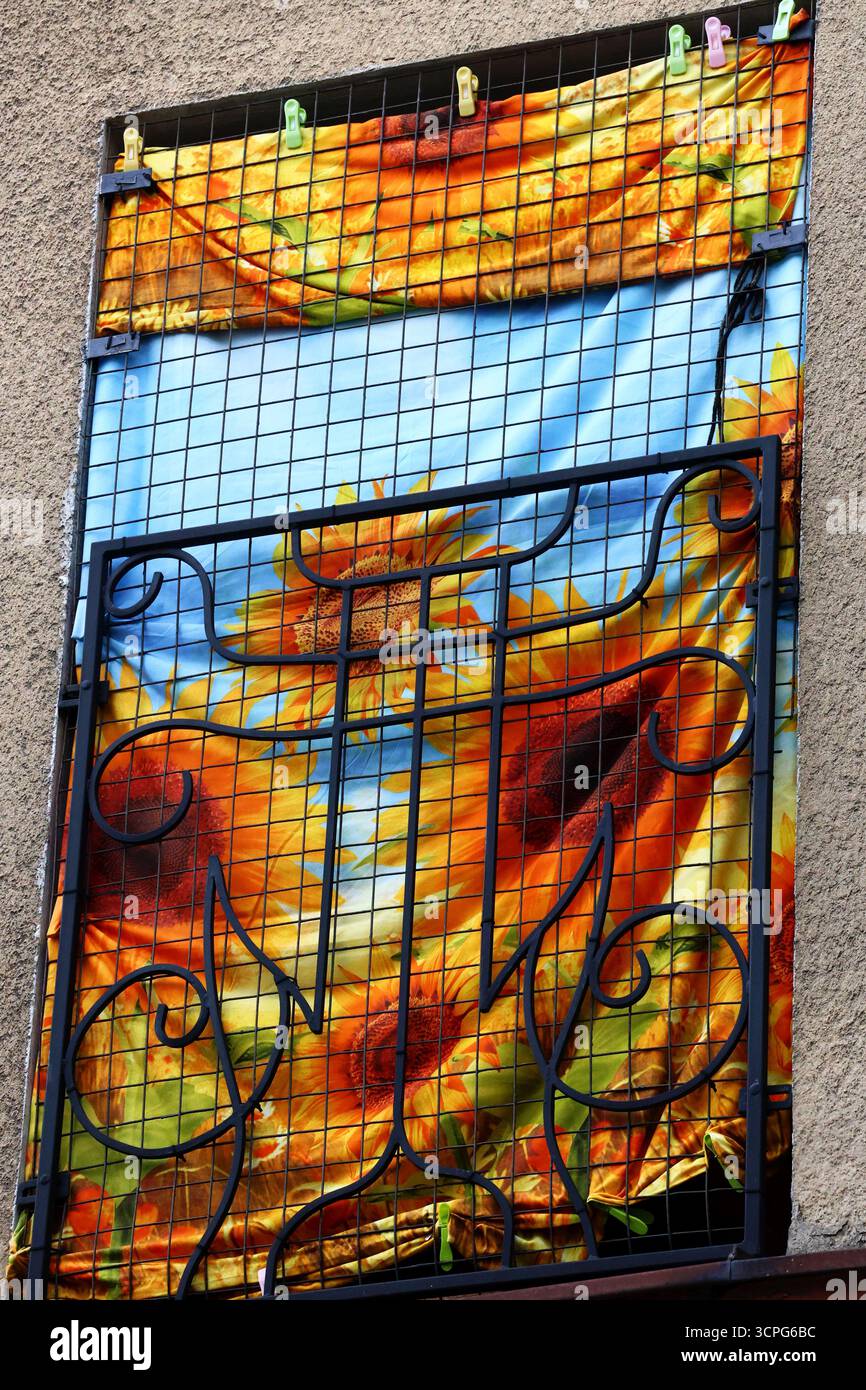 una finestra con una struttura decorativa in ferro ricoperta da un tessuto decorativo e vivace con un motivo floreale Foto Stock