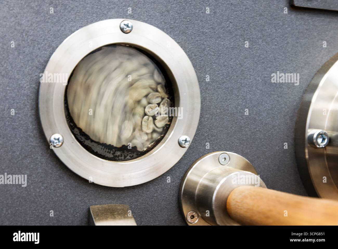 Dettagli di una torrefazione industriale. Foto ravvicinata con semi verdi arrostiti dietro una piccola finestra tecnologica rotonda Foto Stock