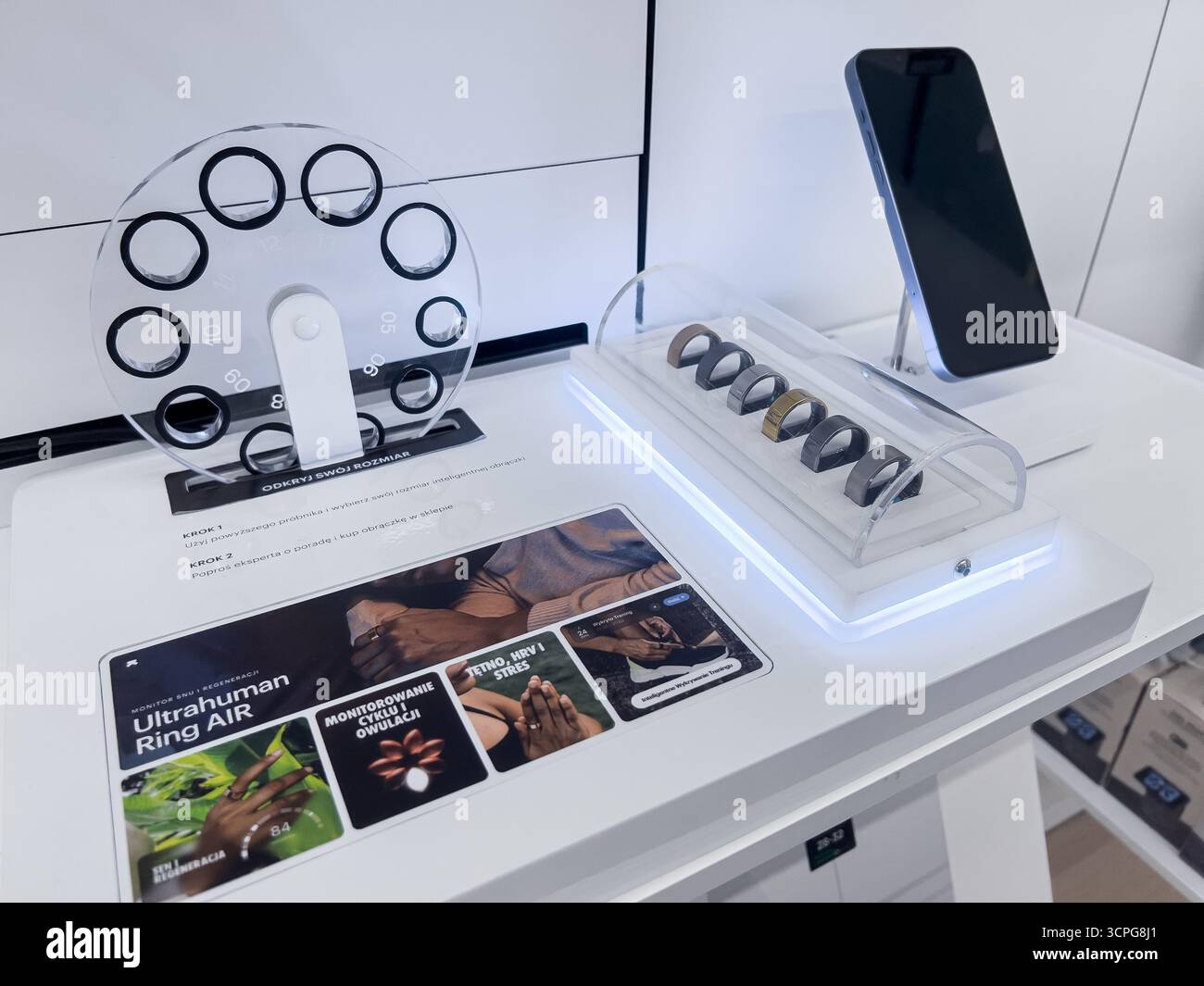 Poznan, Polonia - 20 settembre 2025: Un elegante espositore al dettaglio presenta vari anelli intelligenti, una misura dell'anello e uno smartphone, mettendo in risalto la salute indossabile Foto Stock