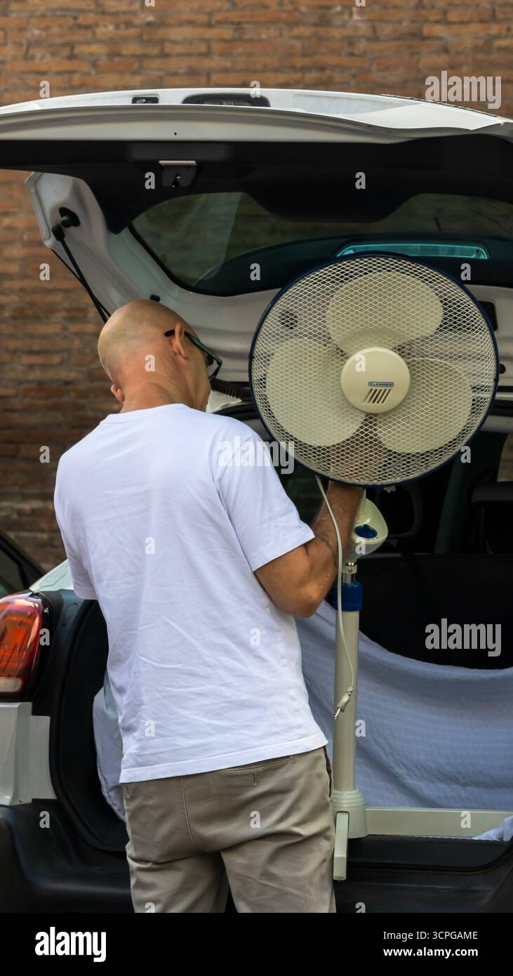 Uomo che trasporta un ventilatore all'interno di un'auto durante un'ondata di calore romana, Foto Stock
