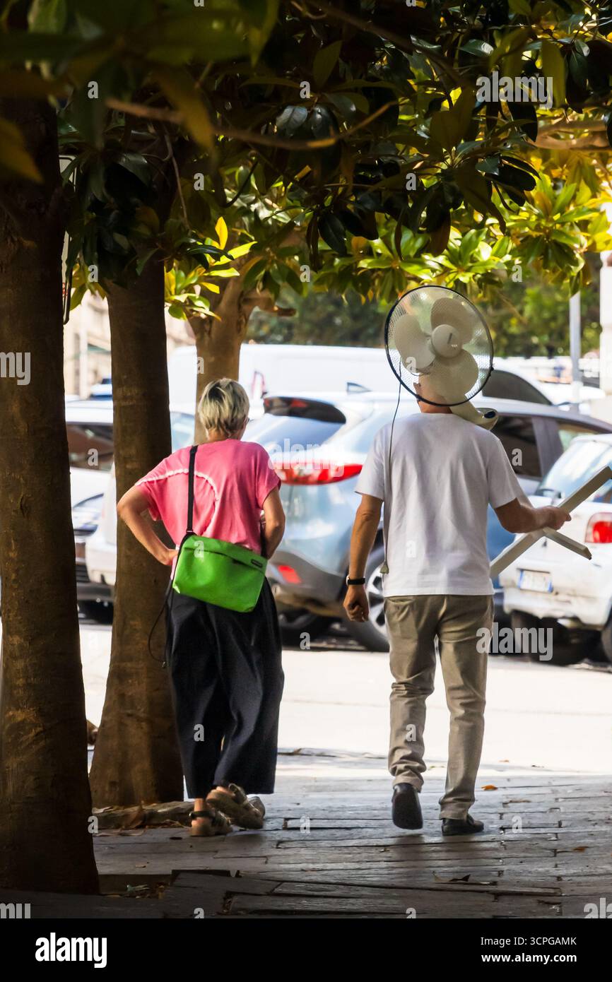 Uomo che porta un ventilatore sulla spalla durante un'ondata di caldo a Roma Foto Stock