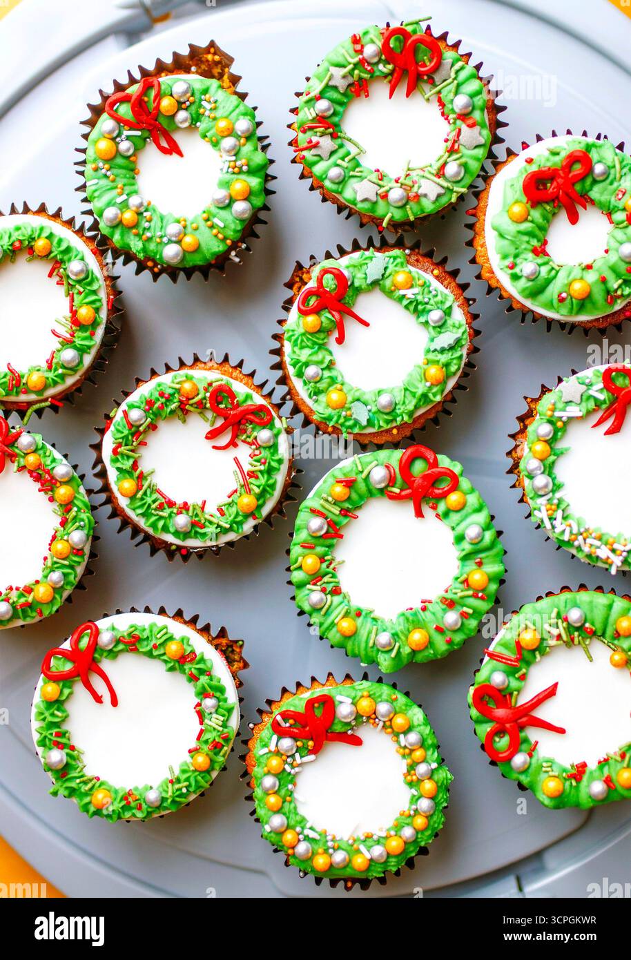 I cupcake festivi sono decorati con disegni colorati di ghirlande, con archi rossi ed elementi decorativi verdi su un piatto grigio Foto Stock