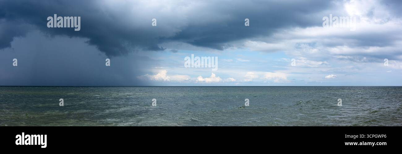 Nuvole di tempesta pesanti e scure si riuniscono sull'orizzonte del mare. Acque verdi e calme prima che il tempo cambi. Foto Stock