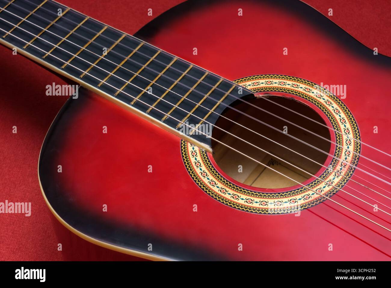 Primo piano di una chitarra acustica rossa, con particolare attenzione alle corde e alla rosetta decorativa. Il vivace colore rosso e il design complesso aggiungono un tocco di eleganza Foto Stock