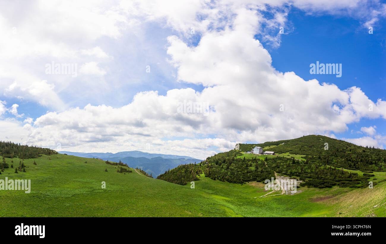 Una vista mozzafiato del Monte Rax in Austria che mostra un paesaggio verde vivace sotto un cielo blu luminoso punteggiato da nuvole soffici Foto Stock