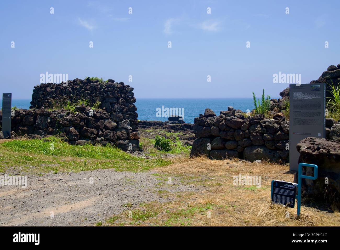 Una pausa nel muro di difesa costiera di Sinsan Hwanhaejangseong si apre verso la costa lavica e il Mare Orientale, con pietre di basalto e segni interpretativi Foto Stock