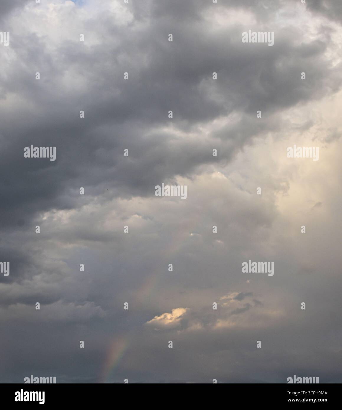 Il cielo regge un arcobaleno vibrante sopra nuvole spettacolari, catturando il contrasto della natura tra luce, colore e oscurità. Foto Stock