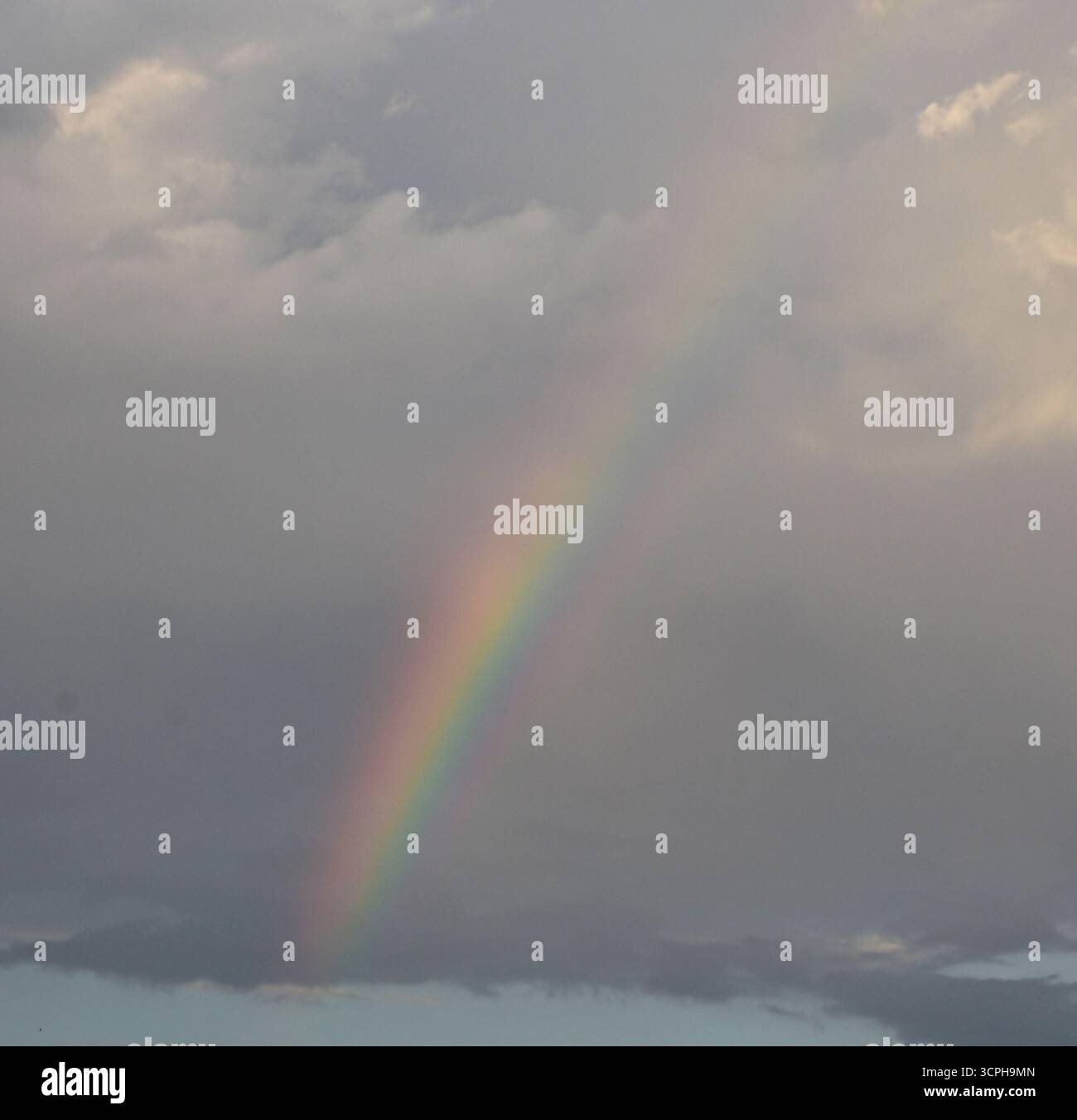 L'arcobaleno etereo appare sopra nuvole morbide e tempestose, colorando il cielo con luce e ombra in gradienti magici. Foto Stock