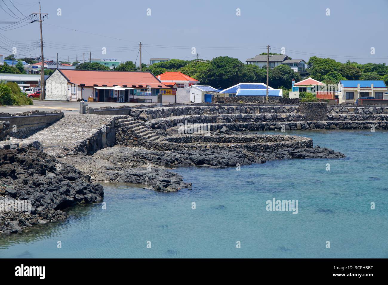 Gradini e banchine terrazzati in pietra conducono ai ristoranti e alle case sul lungomare di Onpyeong, sopra una calma insenatura di acqua azzurra. Foto Stock