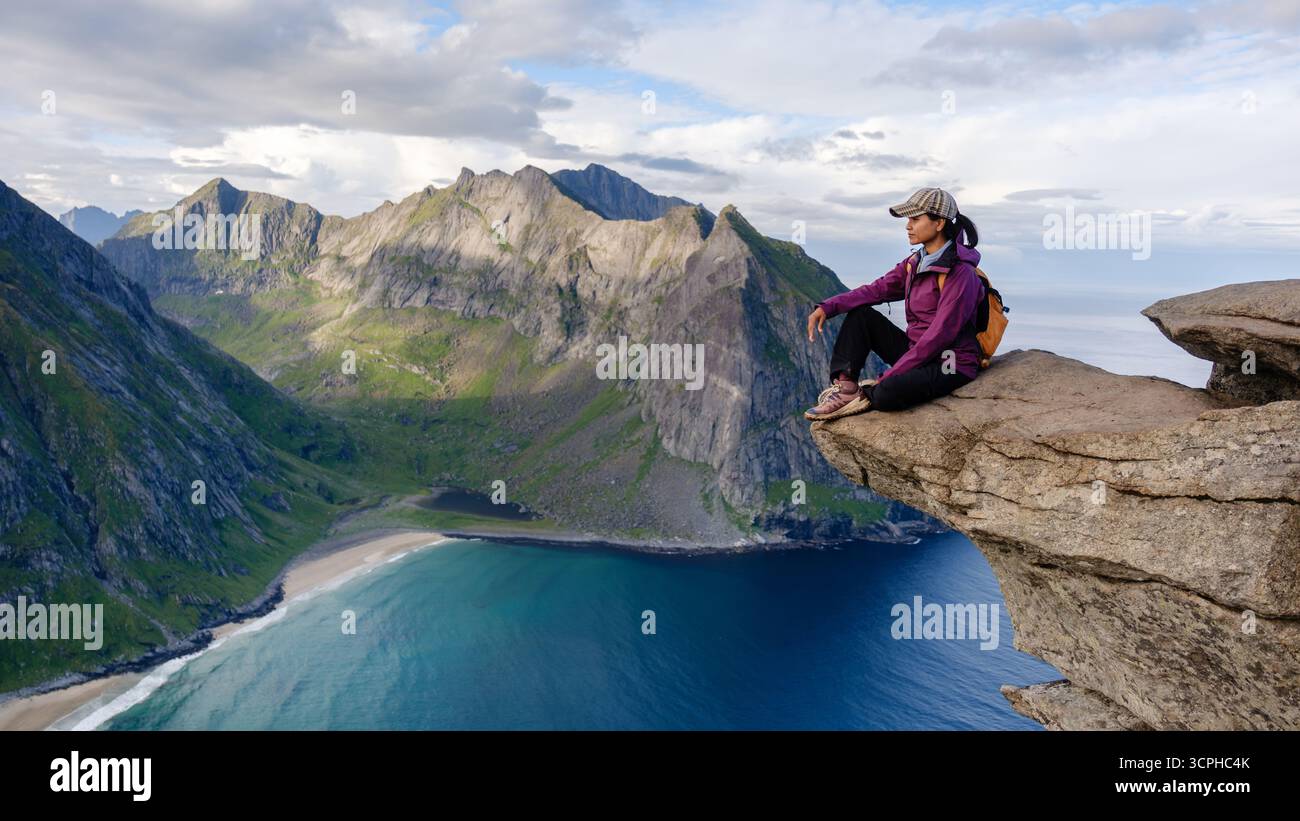 Un escursionista solitario gode di vedute mozzafiato dal punto panoramico di Ryten, affacciato sulla splendida spiaggia di Kvalvika e sulle spettacolari montagne di Lofoten, Norvegia, durante una giornata limpida. Foto Stock