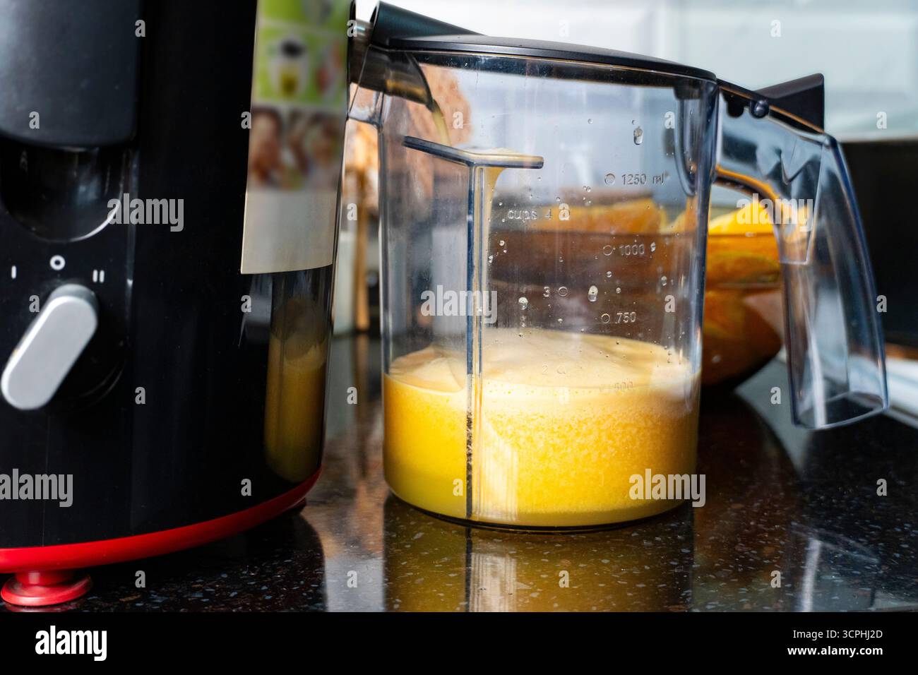 Primo piano della centrifuga elettrica che estrae il succo d'arancia fresco in un contenitore di misurazione, perfetto per uno stile di vita sano e concetti di elettrodomestici da cucina Foto Stock